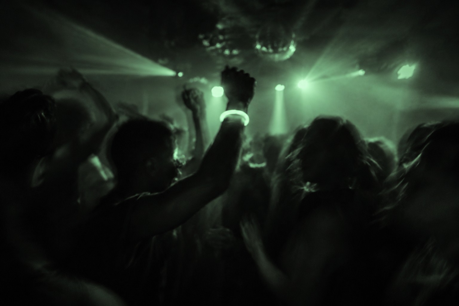 A crowd dancing together beneath green lights